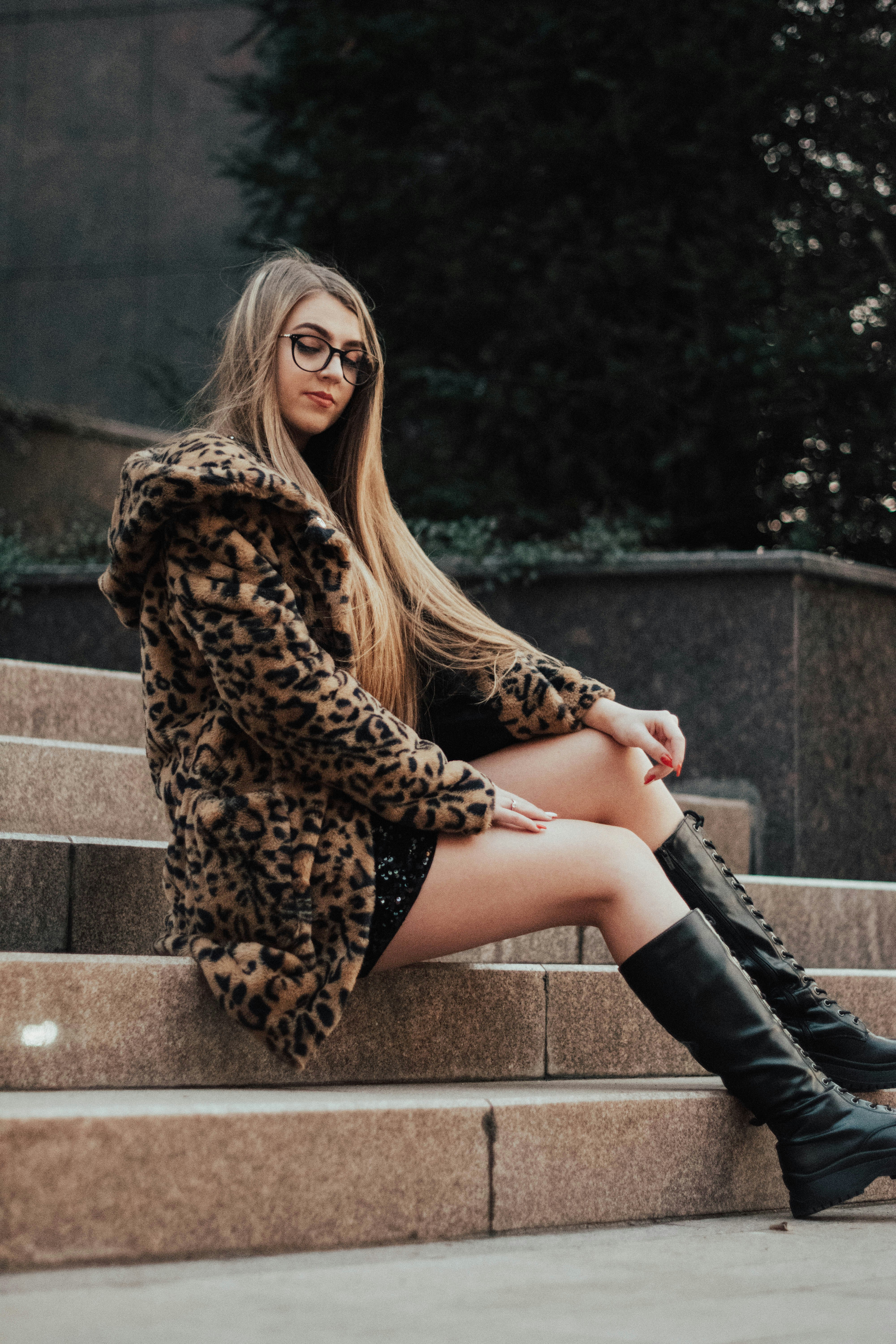 woman in brown leopard print coat sitting on concrete bench